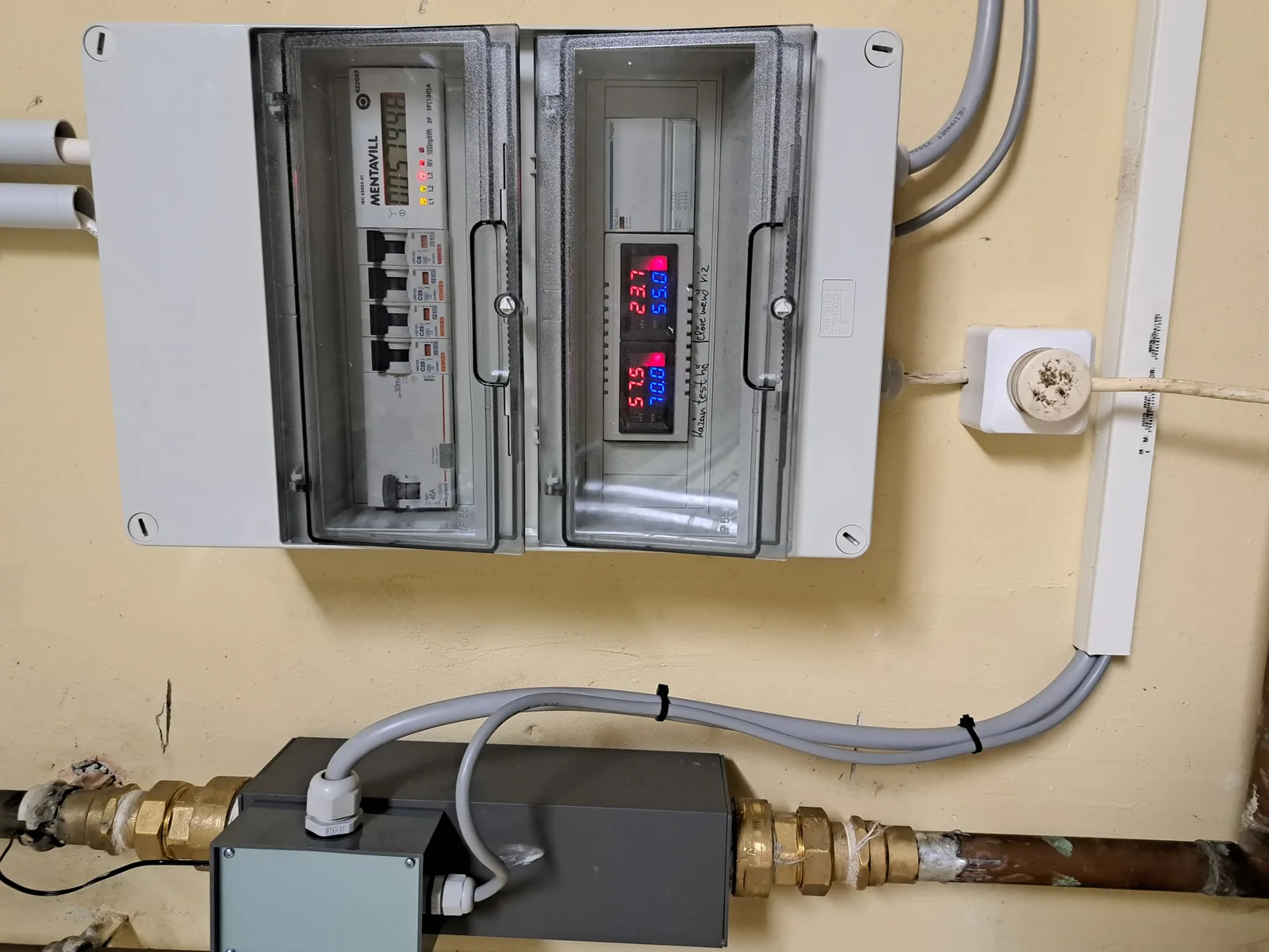 Az AT fűtőmodul egy meglévő rendszerbe kötve: a szürke modul a régi rézcsőbe illesztve, fölötte az elektromos szekrény a fogyasztásmérővel.